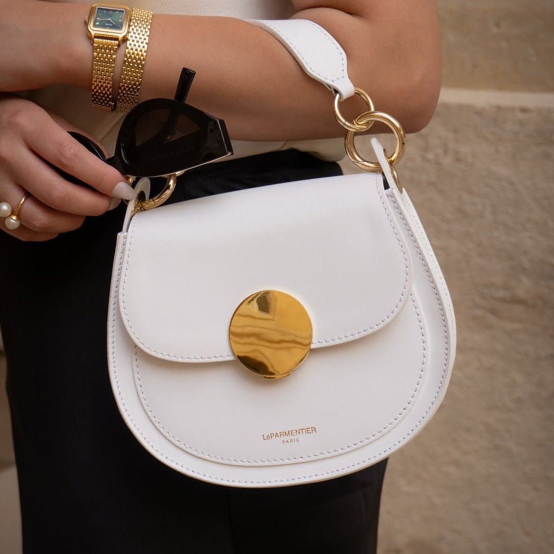White LeParmentier Paris handbag with gold accents held by a person wearing a watch.